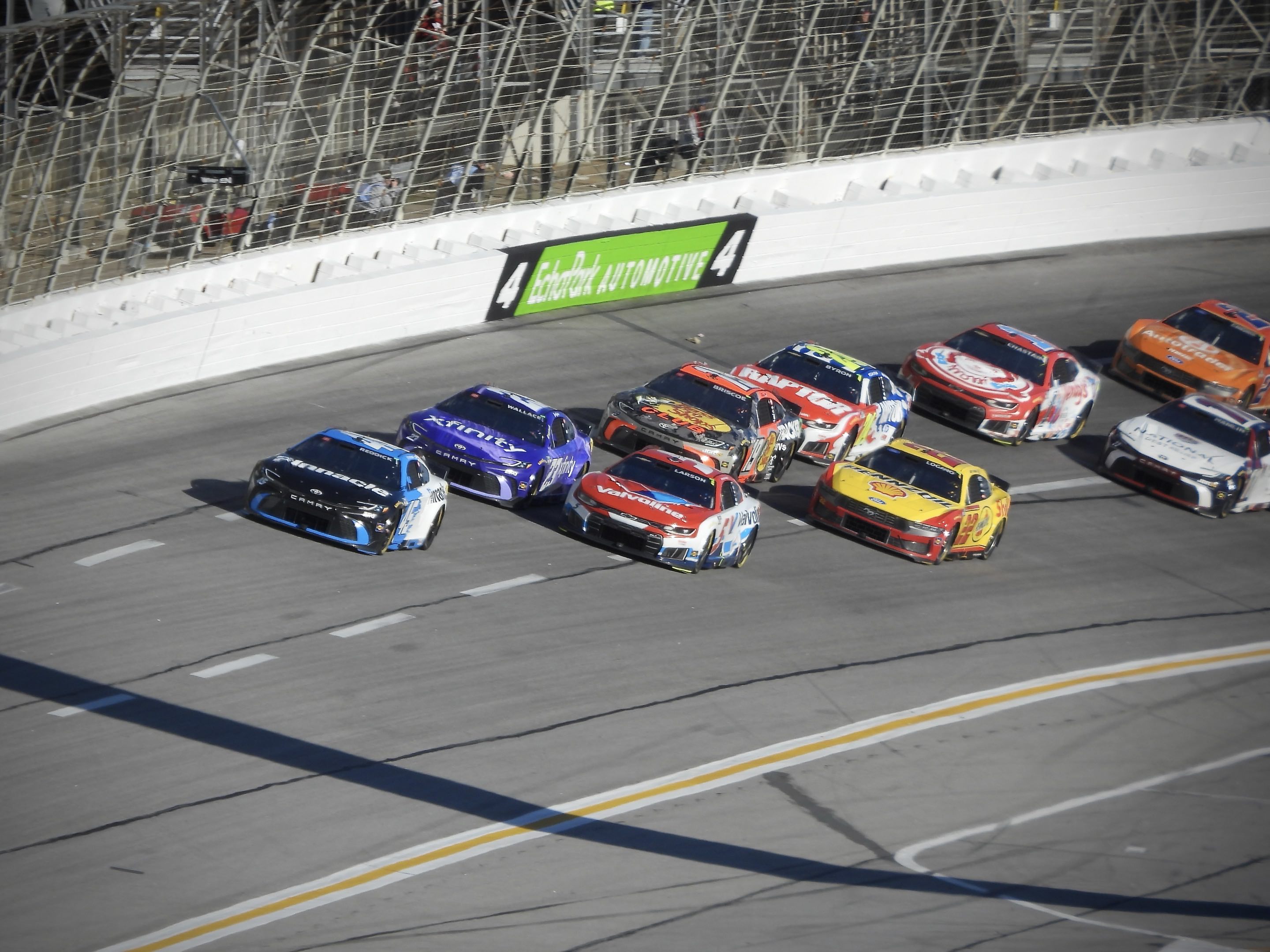 A pack of NASCAR Cup cars racing through turn 4 at EchoPark Speedway in Atlanta with Tyler Reddick being pushed by Bubba Wallace in the lead
